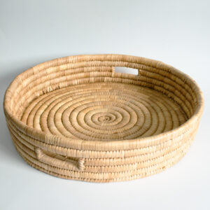 A round, hand-woven tray with a natural brown color and intricate patterns. The tray is made of natural materials and has a slightly raised edge.